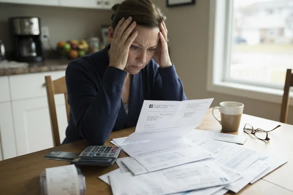 A woman at a kitchen table with her hand on her forehead, looking at an opened repayment letter surrounded by envelopes, a calculator and a coffee mug.